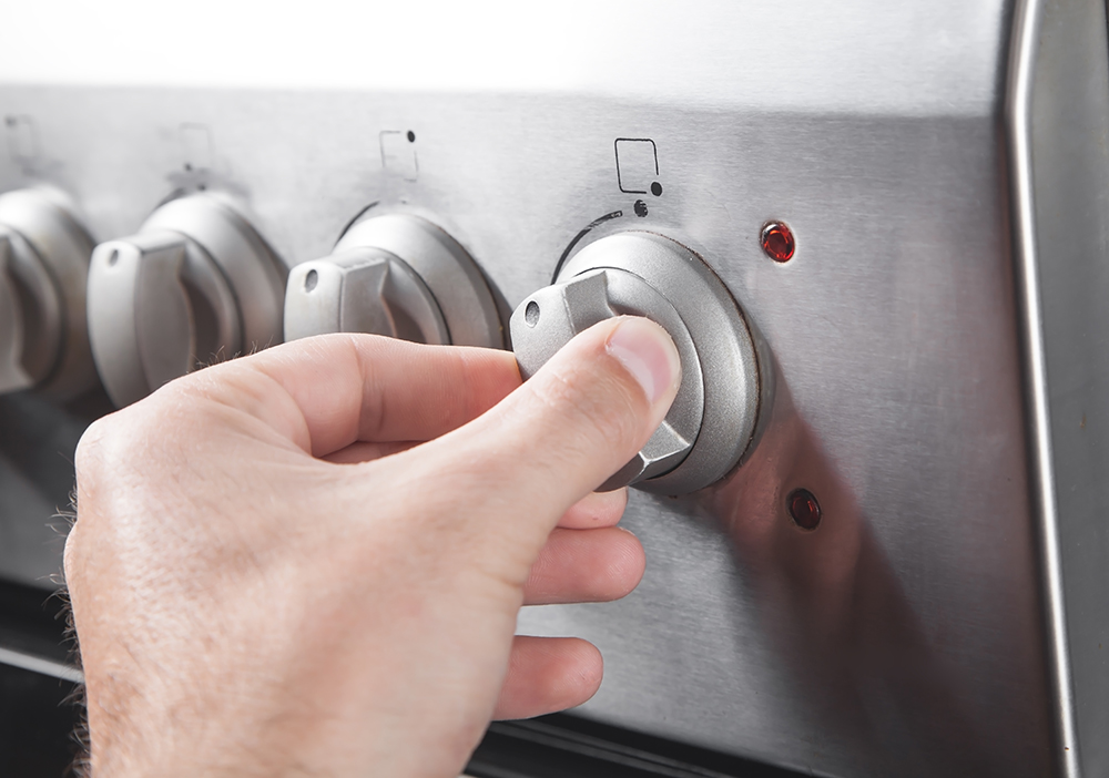 two fingers pinch a stovetop gas range dial