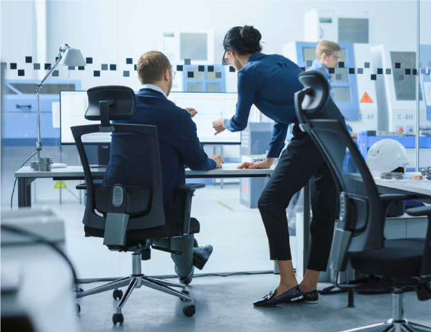 Two office workers in a modern space discuss work on a computer screen